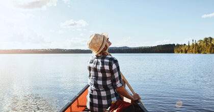Woman in a sun hat canoeing on a Minnesota lake, practicing sun safety to reduce melanoma risk.